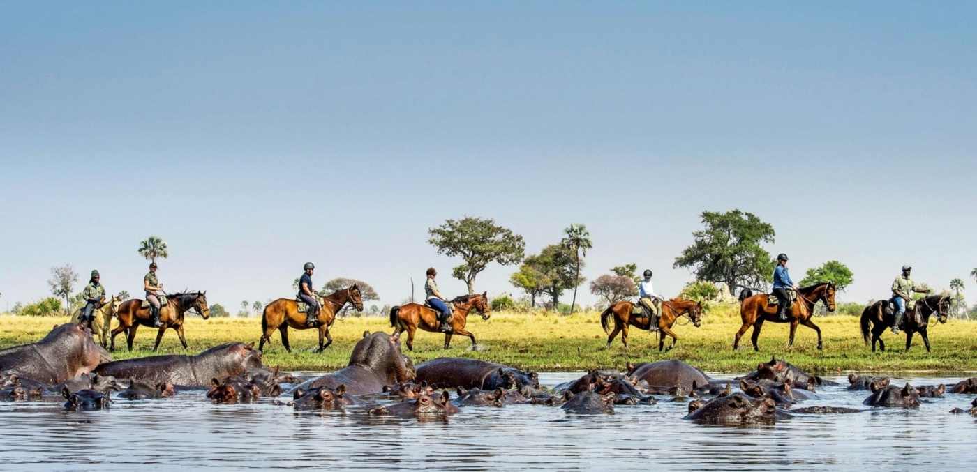people riding horses along river in africa