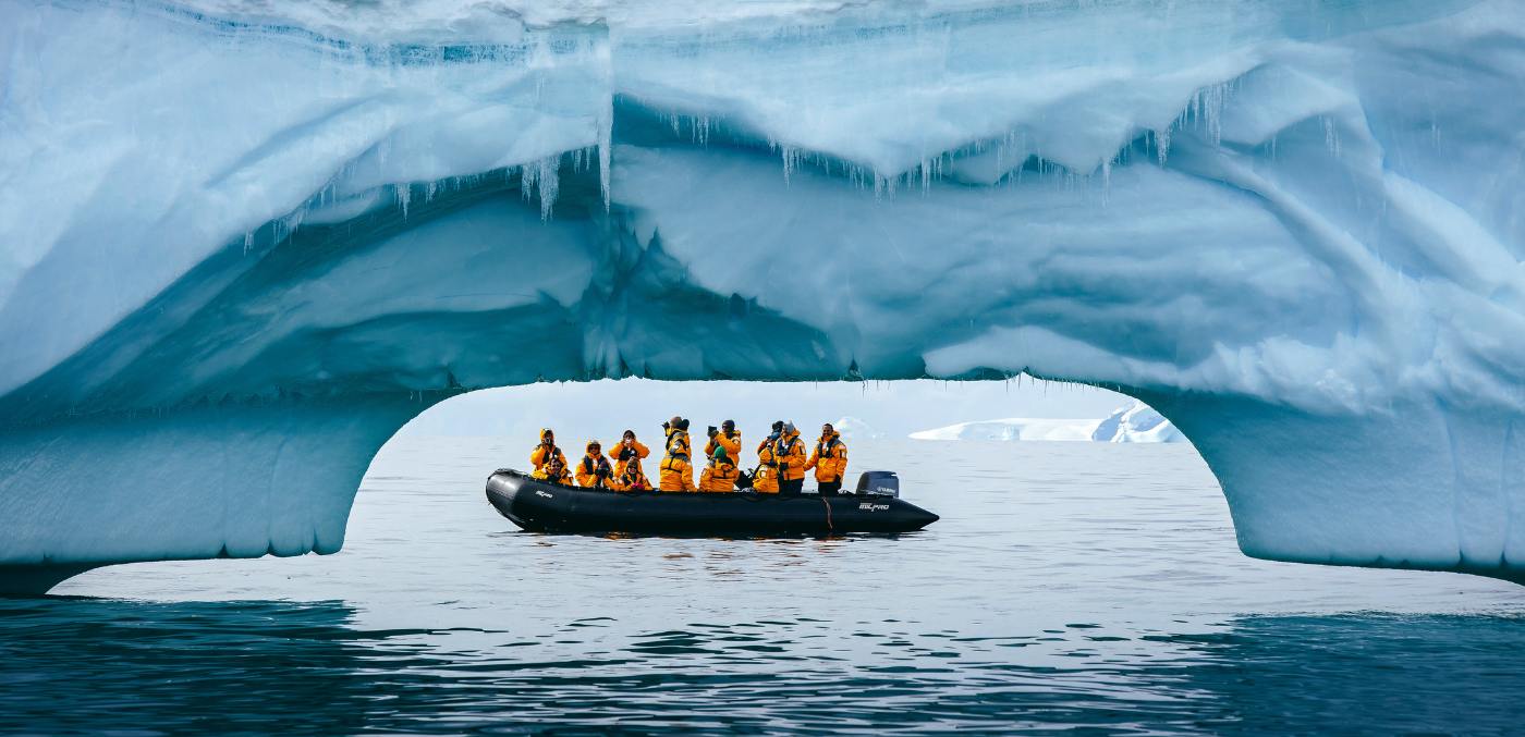 people in long boat floating under ice glacier