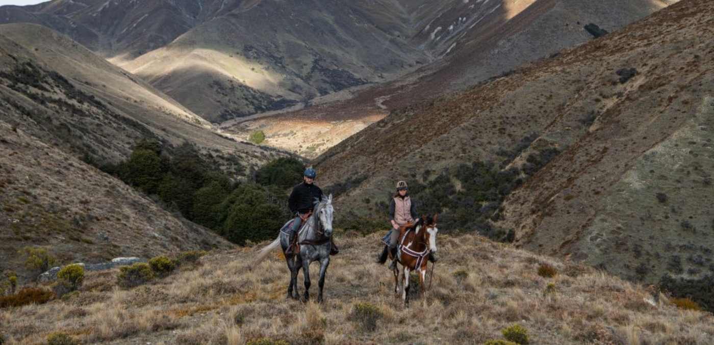 Two people riding horses over hills